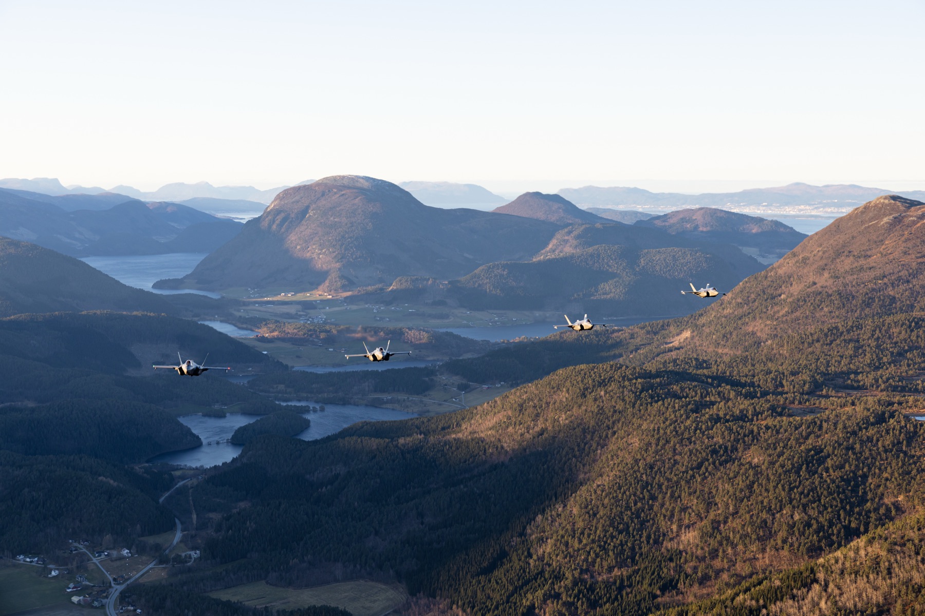 Fire jagerfly flyr over et norsk fjord- og fjellandskap